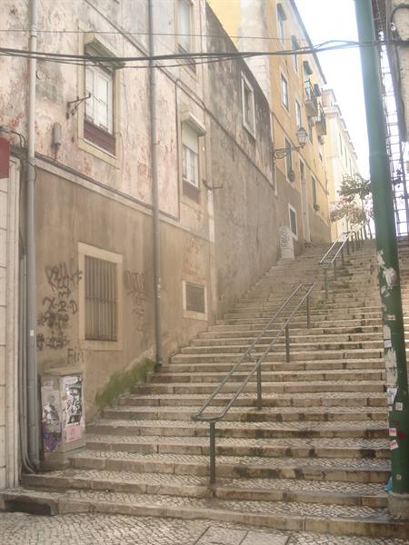 Stone stairway between weathered facades in Lisbon, metal handrails, soft daylight