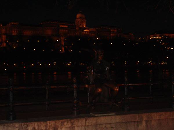 Bronze statue at night by the Danube, Buda Castle illuminated in the background