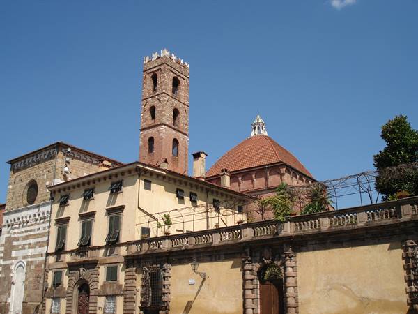 Brick bell tower and terracotta dome above yellow palaces in Lucca