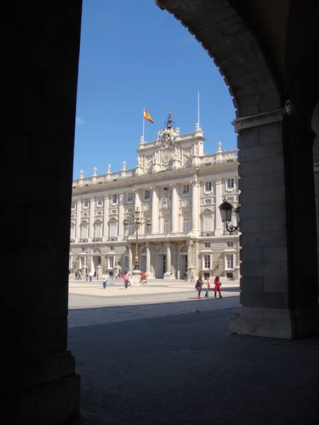 Royal Palace of Madrid framed by a stone arch, Spanish flag flying