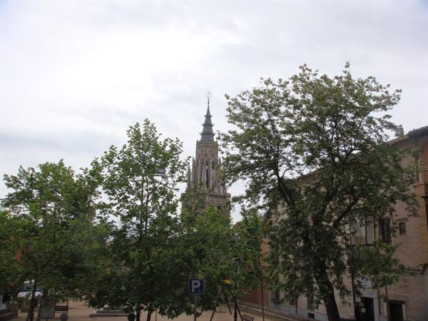 The Gothic spire of Toledo Cathedral rises among trees and buildings