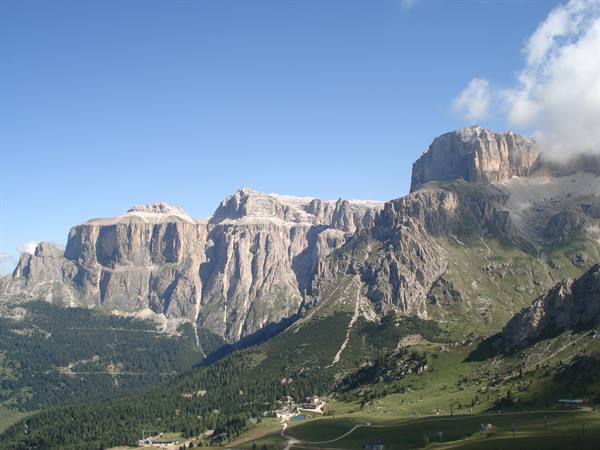 Sella group limestone walls above green meadows and ski lifts, blue sky