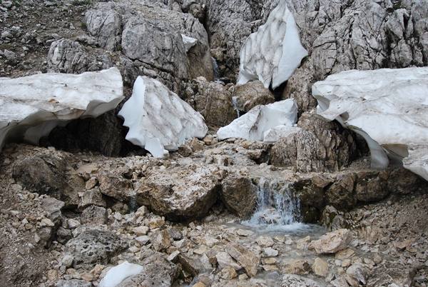 Meltwater stream flows over limestone boulders among patches of leftover mountain snow