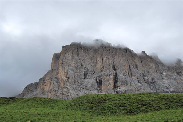 Dolomite rock wall wrapped in clouds above a green meadow