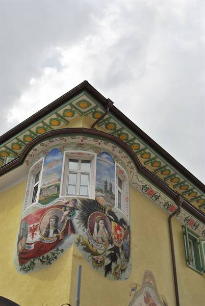 Corner of yellow house with historic frescoes and ornate oriel window, cloudy sky