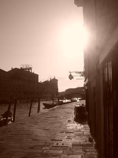 Venice: blazing sun over the canal, moored gondolas, stone embankment