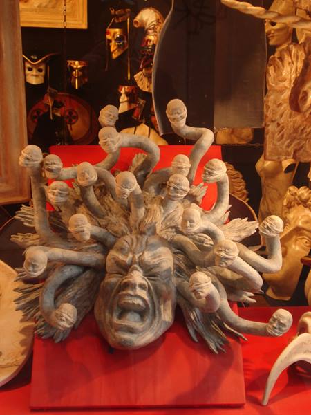 Paper mache Medusa mask displayed in a shop window among carnival masks, warm light