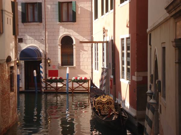 Golden gondola moored along a canal between colorful buildings, direct sunlight