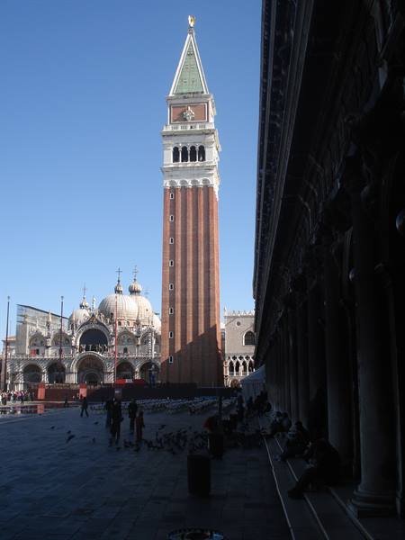 Bell tower and basilica in a Venetian square, sunlight, tourists and pigeons walking