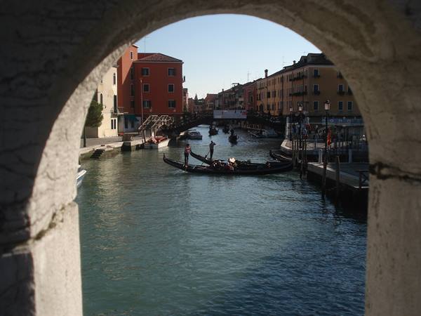 Gondoliers row a gondola across a busy canal framed by a stone arch, Venice