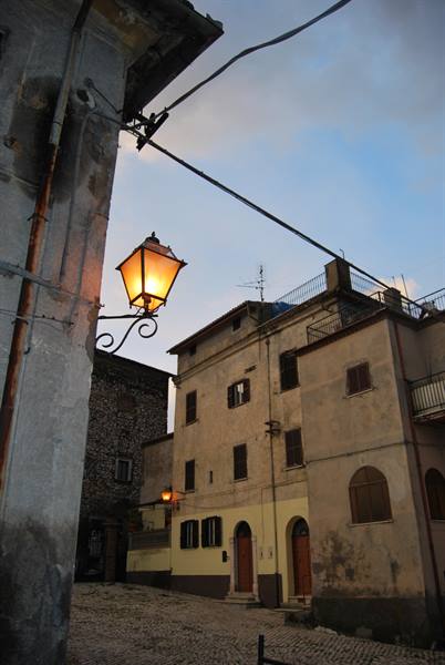 Lit street lamp on old stone houses, evening sky