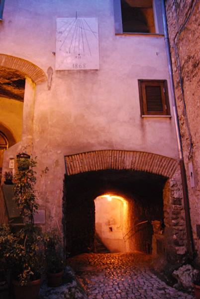 Brick arch over cobbled alley, painted sundial, warm light under the passage
