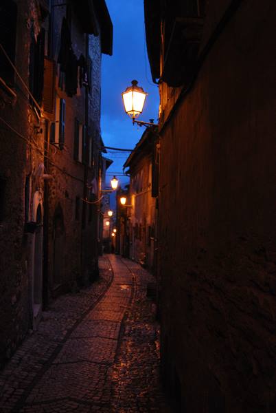 Cobblestone alley wet at night, glowing street lamps between stone houses