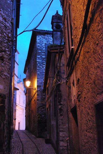 Cobbled alley between stone houses at dusk, lit street lamp