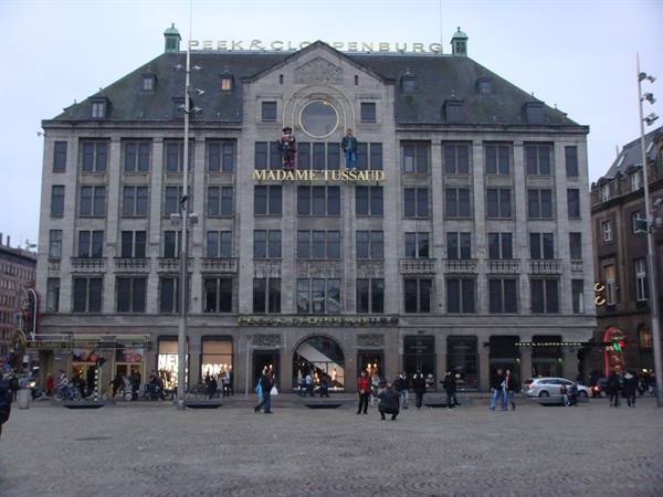Madame Tussauds stone facade on Dam Square, Amsterdam, pedestrians and cyclists under grey sky