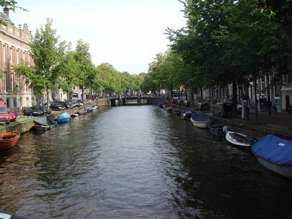 Boats moored along an Amsterdam canal, brick houses and a bridge