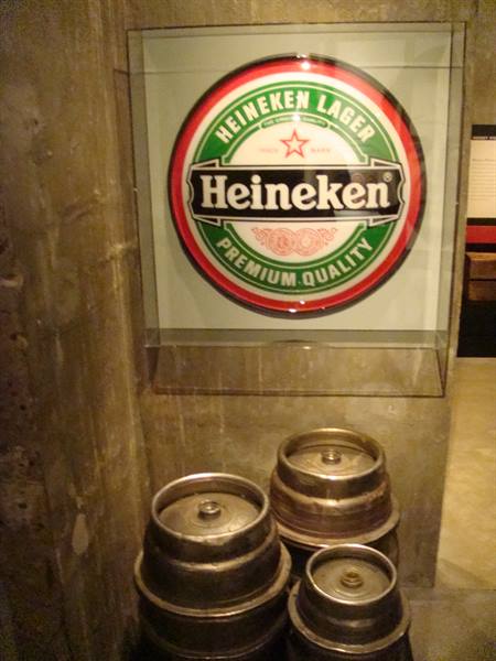 Heineken sign behind glass with old metal beer kegs below