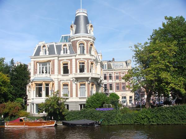 Historic villa with tower overlooking the canal, wooden boats moored, Amsterdam
