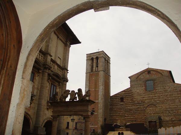 Cathedral bell tower and stone palace in Montepulciano, framed by a stone arch