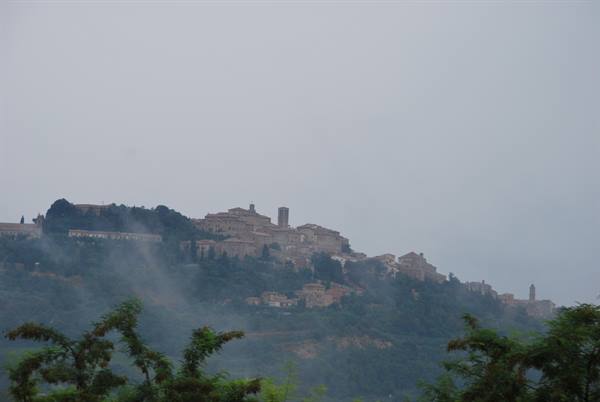 Montepulciano wrapped in mist, stone houses crowding the wooded hilltop