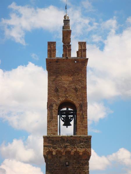 Brick bell tower with bronze bell against white clouds