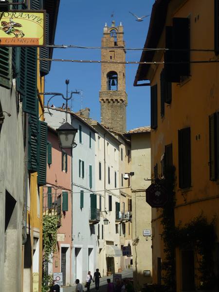 Brick bell tower above colorful houses in Pienza, shadow and sunlight