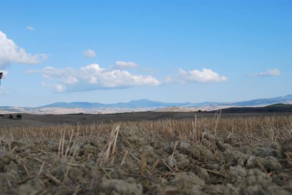 Plowed stubble fields near San Quirico d'Orcia, rolling hills and white clouds