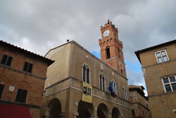 Pienza, travertine town hall with brick bell tower under cloudy sky