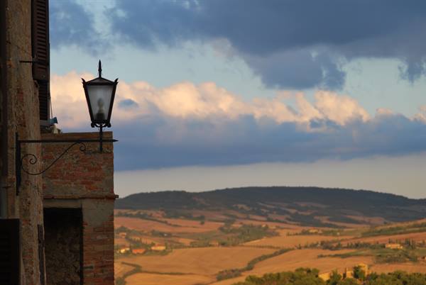 Wrought iron lantern on brick wall, cultivated hills of Val d'Orcia, Pienza