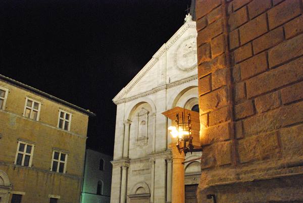 Pienza cathedral facade lit at night among stone buildings