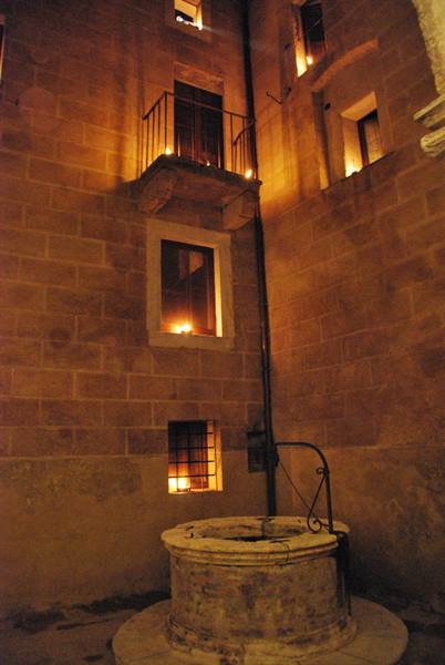 Stone well in medieval courtyard, candlelit windows glowing on the facade