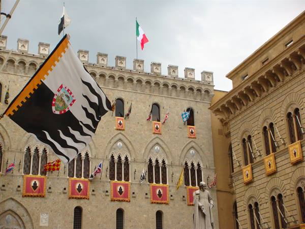 Siena, Piazza Salimbeni: Gothic stone palace with contrada flags and statue