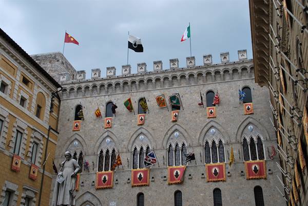 Flags hanging on the gothic facade of Palazzo Salimbeni in Siena