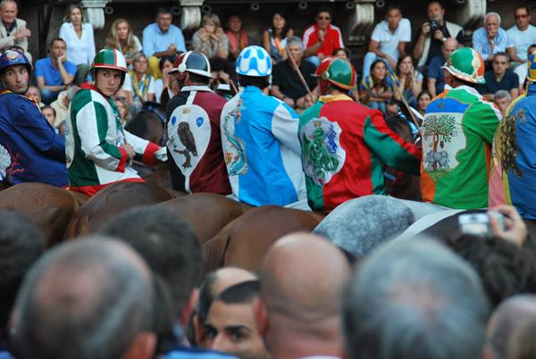 Jockeys in colorful jerseys on horses at the Palio of Siena, cheering crowd