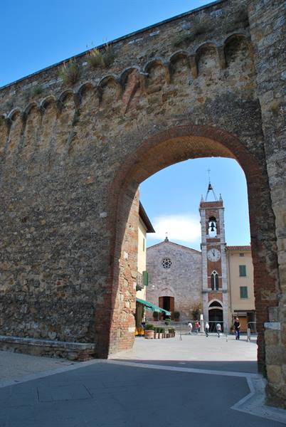 Medieval stone and brick gate framing church and bell tower, San Quirico d'Orcia
