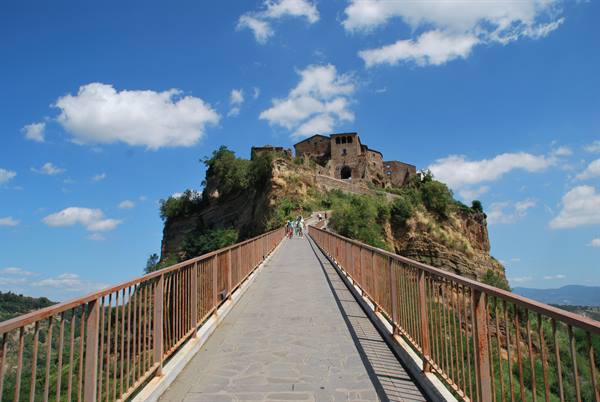 Footbridge leading to Civita di Bagnoregio, ancient houses atop the cliff under a cloudy sky