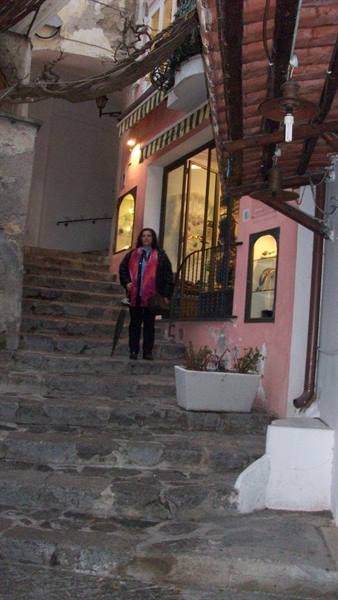 Woman under a brick arcade on stone steps before a pink shop