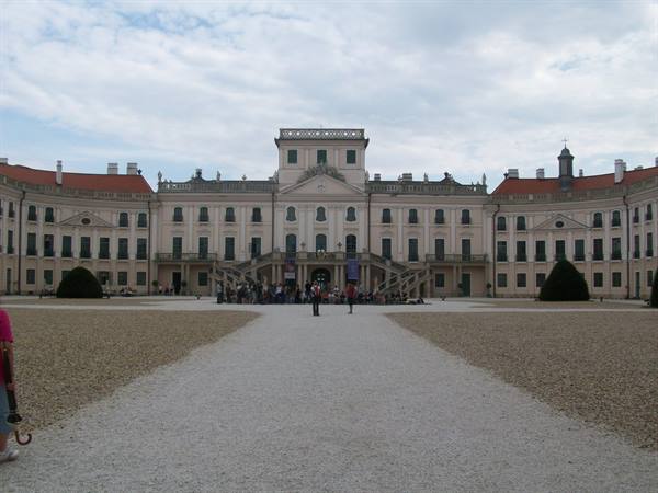 Baroque facade of Fertőd castle with visitors on gravel path under cloudy sky