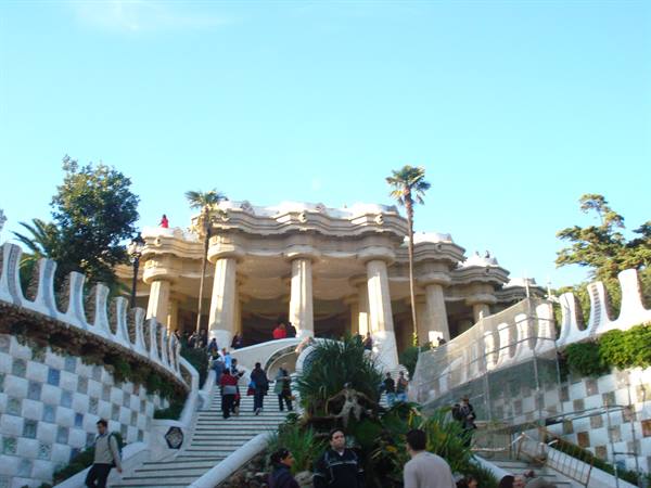 Tourists on Gaudí's stepped terrace at Parc Güell, stone columns and palm trees