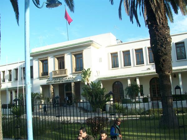 White city hall building with red flag, palm trees and people by the fence