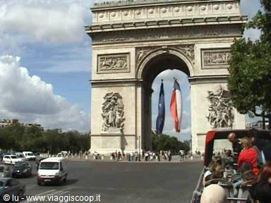 Arc de Triomphe in Paris with French flag, tourists and traffic under cloudy sky