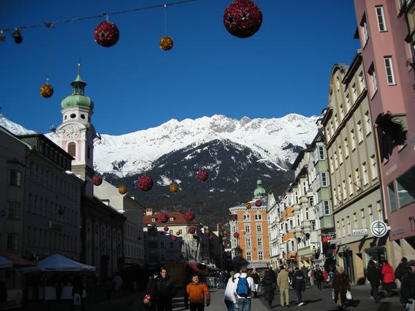 Christmas ornaments hang above the crowd on Maria-Theresien-Straße, Innsbruck, snowy Alps behind