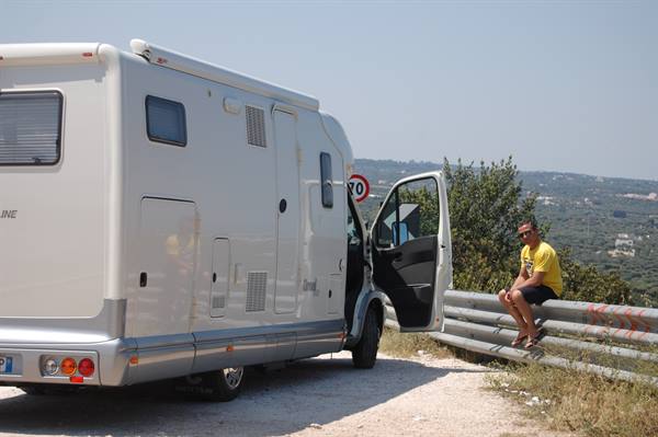 White motorhome parked on gravel, door open, man sitting on the guardrail