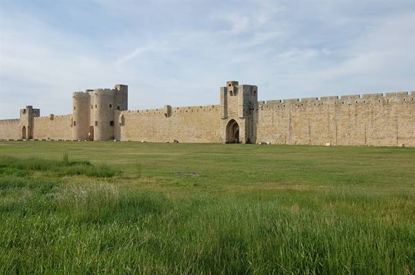 Medieval stone ramparts of Aigues-Mortes, towers and gate under cloudy sky