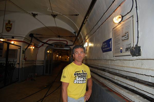 Man in yellow t-shirt inside an underground fort tunnel with rails and pipes