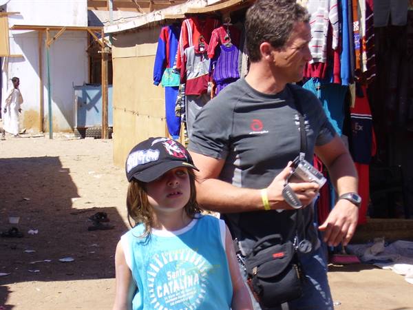 Girl in cap and man with camera walking past stalls of hanging clothes
