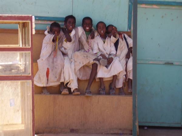 Boys in white robes sitting on wooden steps in front of a green door