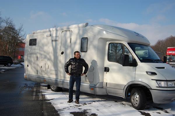 Man in black jacket standing beside a white motorhome on snowy road