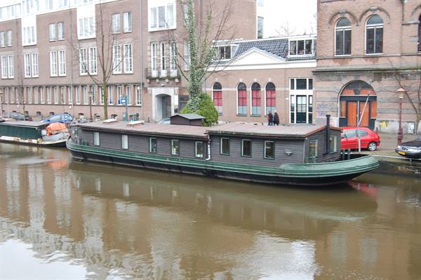 Green houseboat moored along a canal between brick buildings