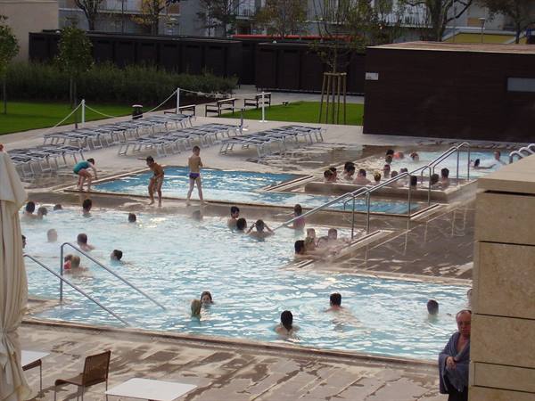 Bathers in outdoor thermal pools, empty loungers and rising steam